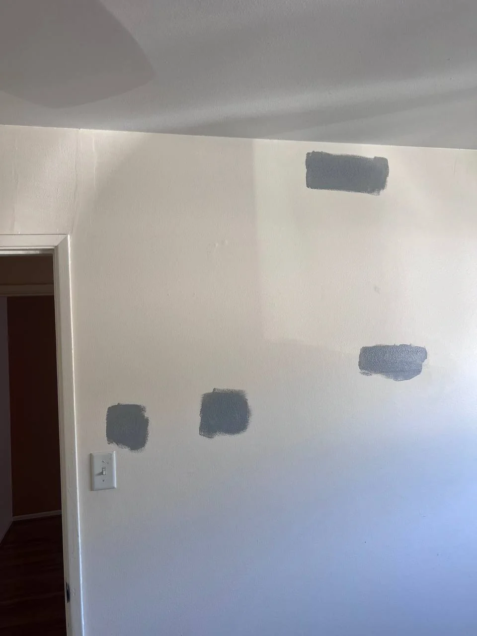 Drywall patches before final paint in a San Diego home — gray joint compound covering anchor and screw holes on a white wall