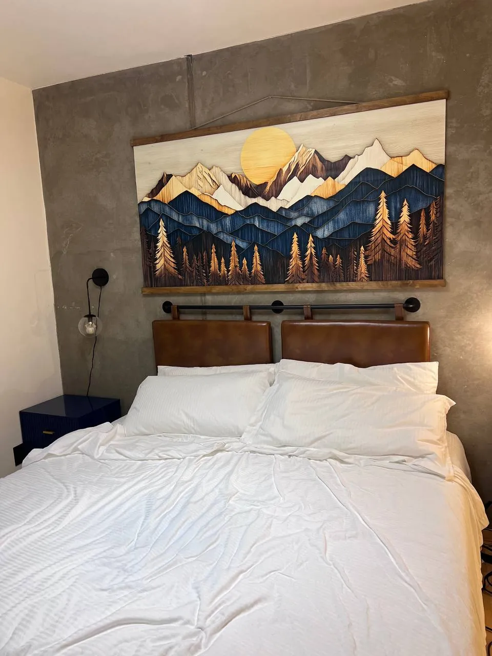 Made bed beneath a mountain mural headboard wall