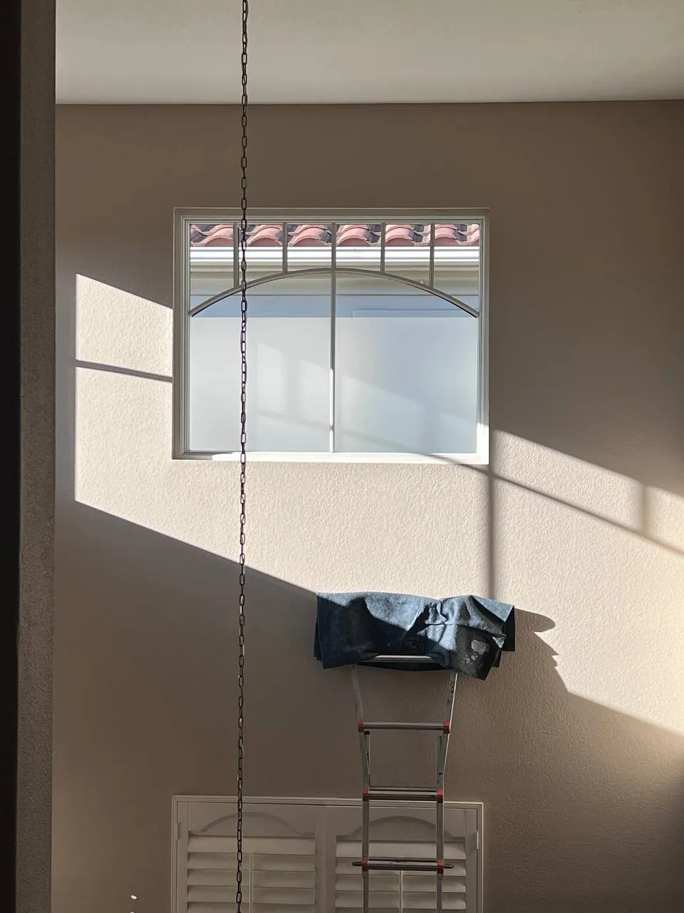 Handyman installing a chandelier from a tall ladder in a stairwell
