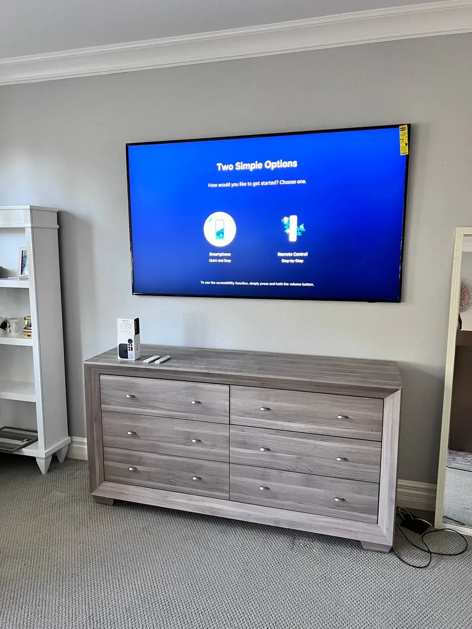 Smart TV wall-mounted above a wood dresser in a bedroom